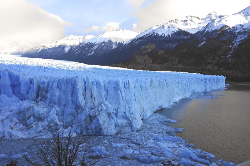 glacier face near an icy lake with snowy mountains beyond, glacier and lake 4k
