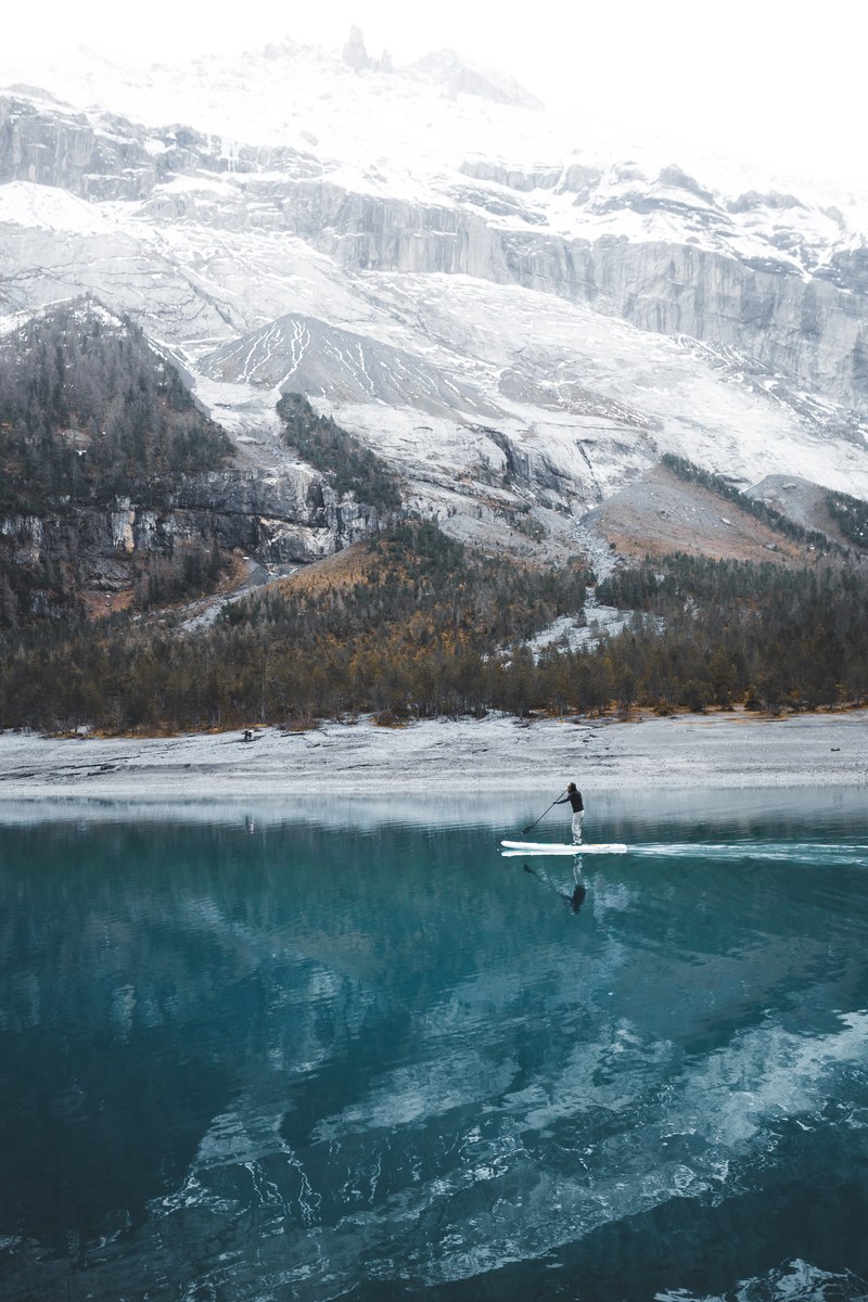 a man on a paddle board on an azure lake in the mountains, paddling on the lake 4k