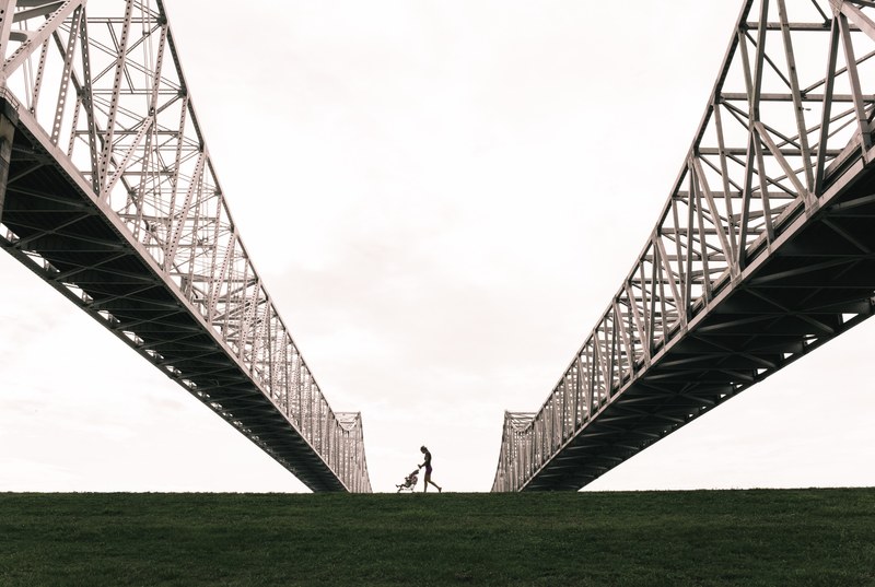 a mother pushing a stroller between the steel arches of a suspension bridge in new orleans, stroller under the suspension bridge 4k