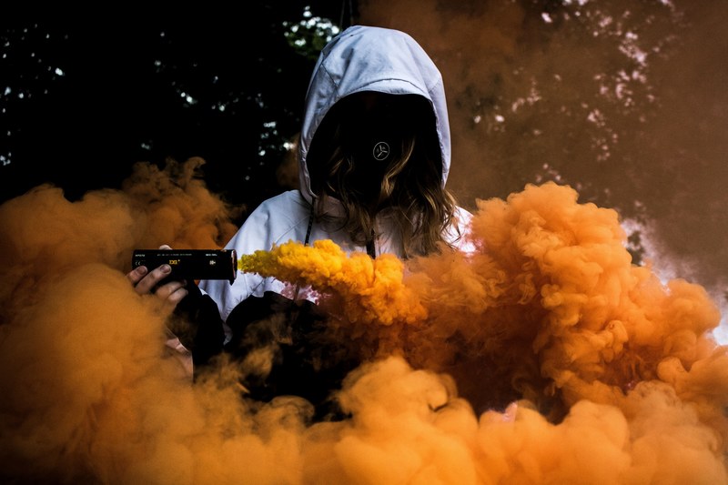 a hooded person is surrounded by orange smoke from a smoke grenade in mostyn, orange haze 4k