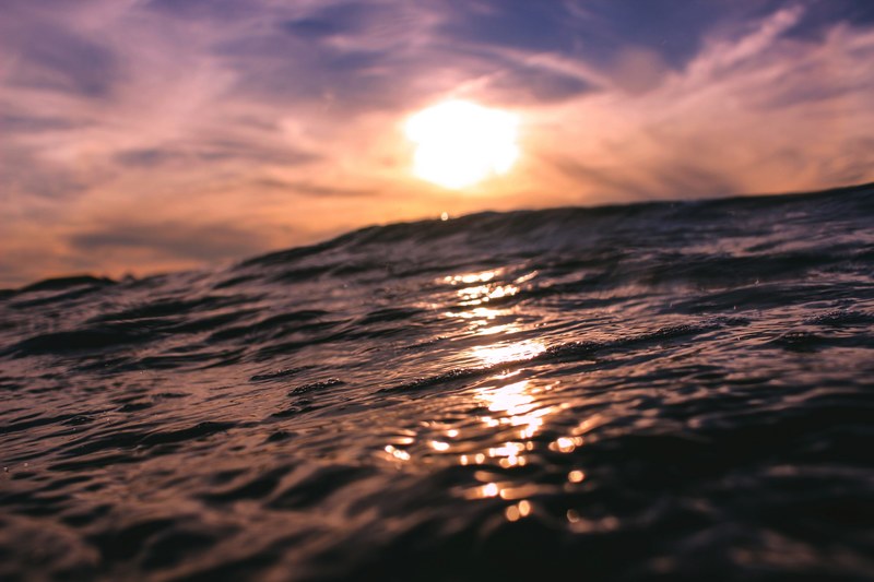 open water underneath swirling clouds and beaming sun, sunrise reflecting over ocean 4k