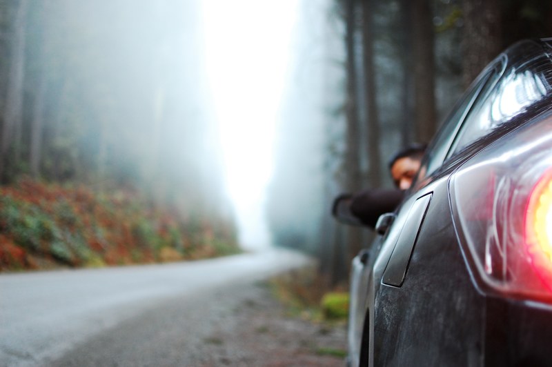 a man leaning out of a window in a car parked on the side of a tree lined road, man looking out of car window 4k