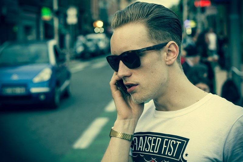 man with a trendy haircut and rayban sunglasses talking on the phone in the city, making a call 4k