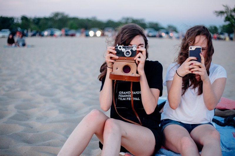 two female friends are taking photos with a vintage camera and a smartphone at the beach, _two phones 4k