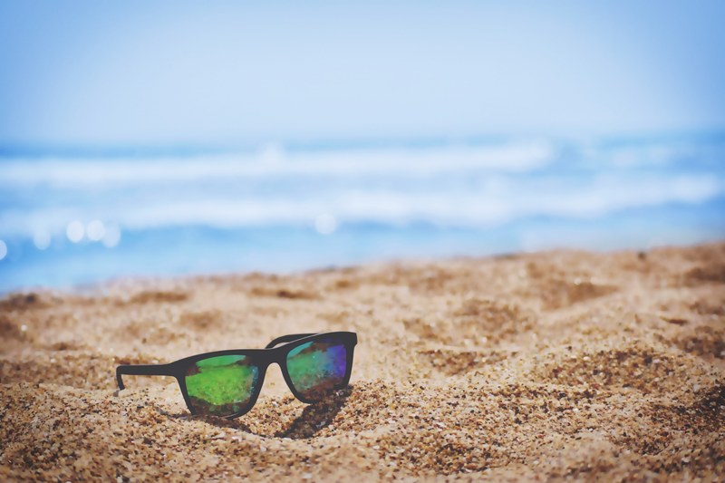 colorful reflections in a pair of sunglasses left on a golden beach, at the beach 4k