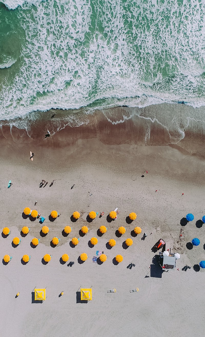 an aerial shot of a sandy beach with rows of yellow and blue umbrellas, cocoa beach vibes 4k