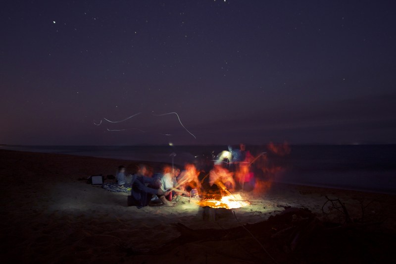long exposure of a group of friends hanging around a beach bonfire lighting the dark night, yellow 4k