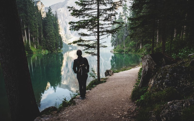 a woman on a path along a still lake in the mountains, on a lakeside path 4k