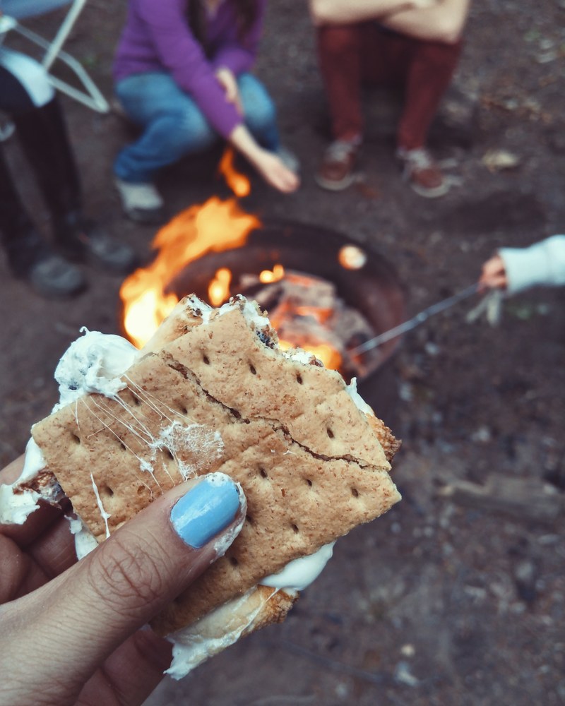 close up of the hand of a woman holding a piece of smore at a campfire, _campfire treats 4k