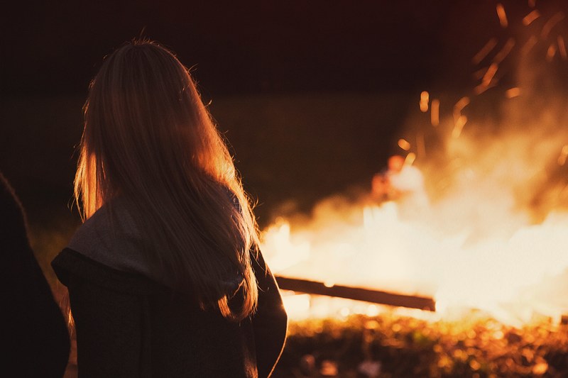 blonde female captured watching a burning campfire, enjoying the campfire_ 4k
