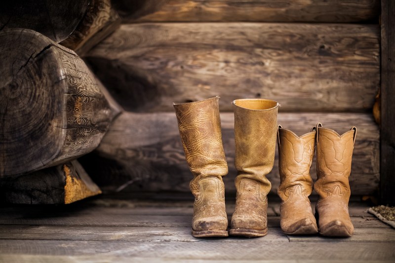 two pairs of worn in cowboy boots set in front of wooden logs, cowboy shoes in a cabin 4k
