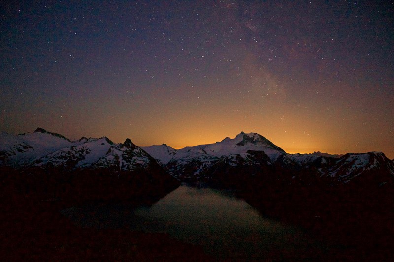 orange glow of the sun peeking from behind snowy mountain ridge stars twinkling above, looking to the stars 4k