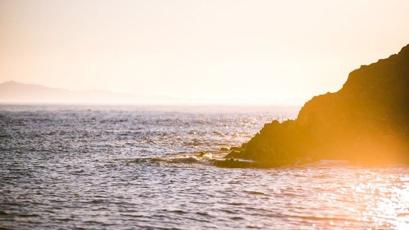 a sunset or sunrise scene over a rock formation and tranquil sea, sunset over the sea and rocks 4k