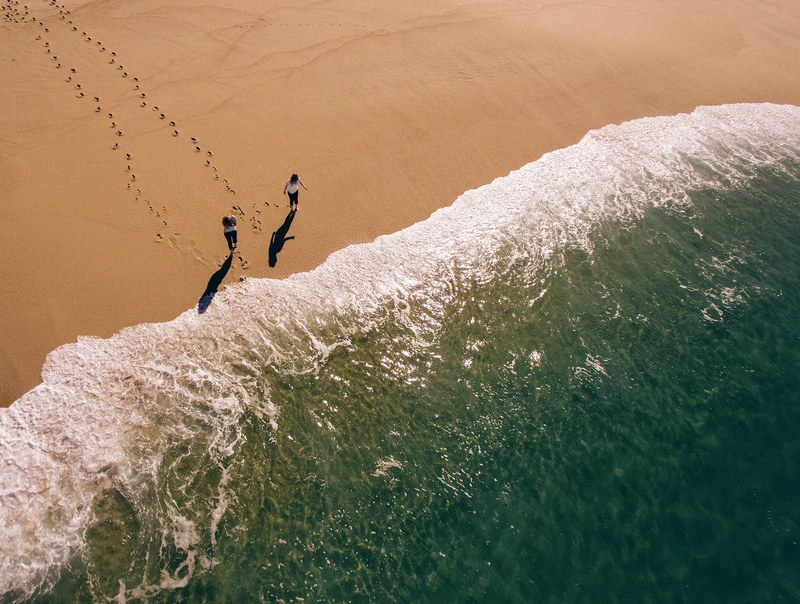 a drone shot of two women walking towards the sea and leaving footprints in the wet sand, friends on a quiet beach 4k