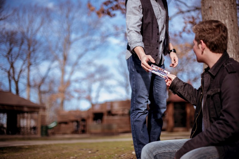 a standing person in a vest hands a ticket to a seated man outdoors, handing over a ticket 4k