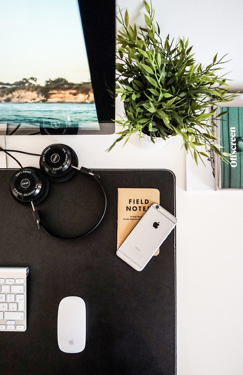 a flatlay with an iphone headphones and a field notes notebook next to a computer display, flatlay with a small notebook 4k