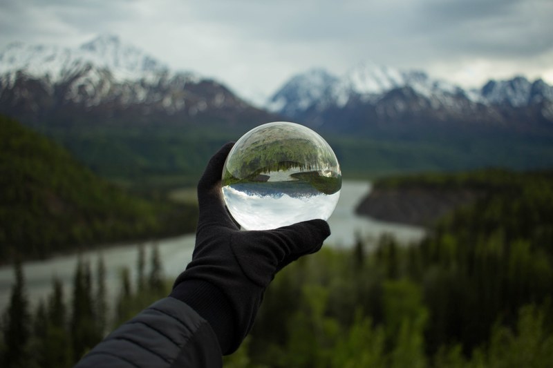 a persons hand in a glove holding a large glass ball against the backdrop of snowy mountains, unfathomed beauty 4k