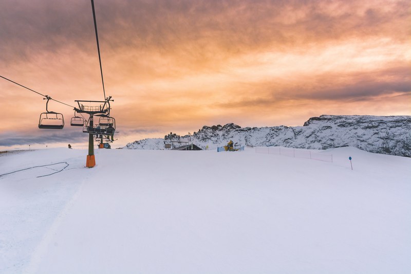 chair lifts on top of a snowcapped seiser alm with an orange cloudy sunset in the distance, sunset over the piste 4k