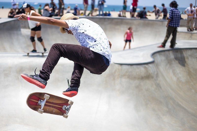 a man wearing a white shirt and hat doing tricks on a skateboard at a skatepark, skateboard trick in park 4k