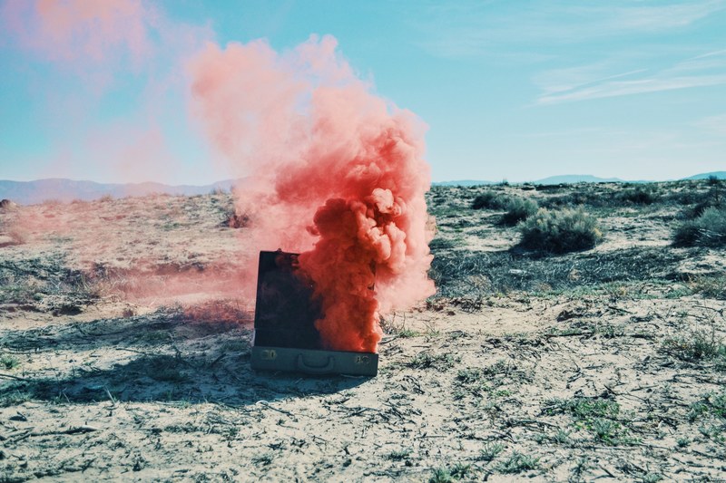 red smoke billows from a suitcase in a sandy desert, pink smoke in the desert 4k