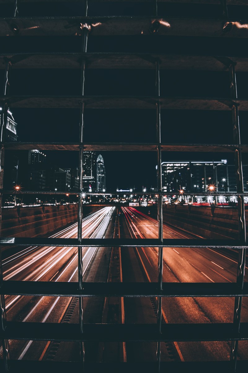 a view of passing headlights on a cincinnati at street from behind a building grill, traffic at night in cincinnati 4k