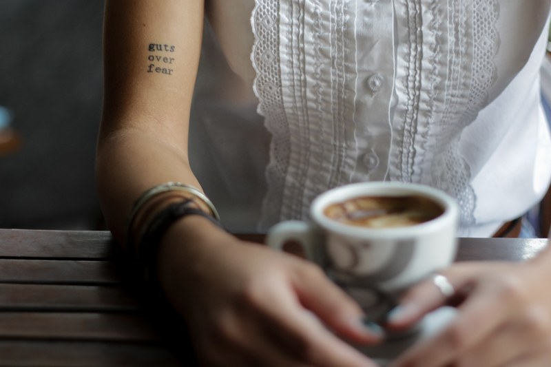 a woman with a guts over fear tattoo sitting over coffee, guts over fear 4k