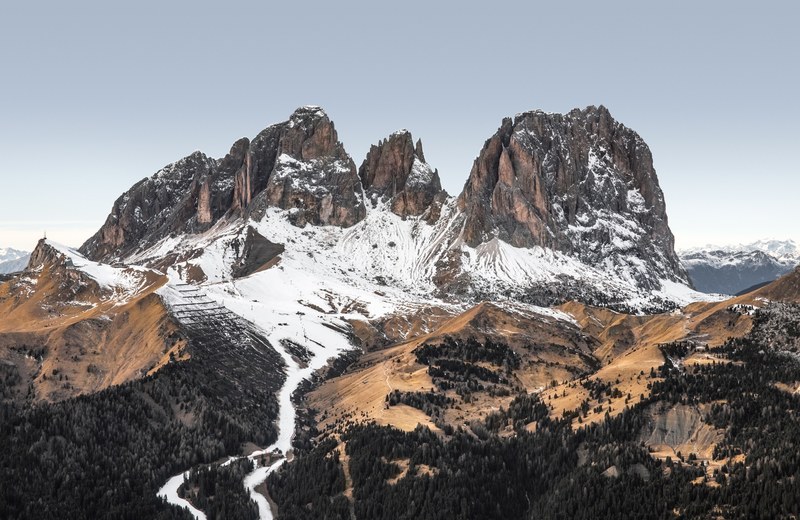 jagged rock towers rising up above wooded hills in italy, passo sella dolomites 4k