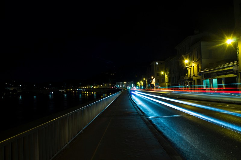 light from car speeds past on a city road near the water at night, walking path by the road 4k