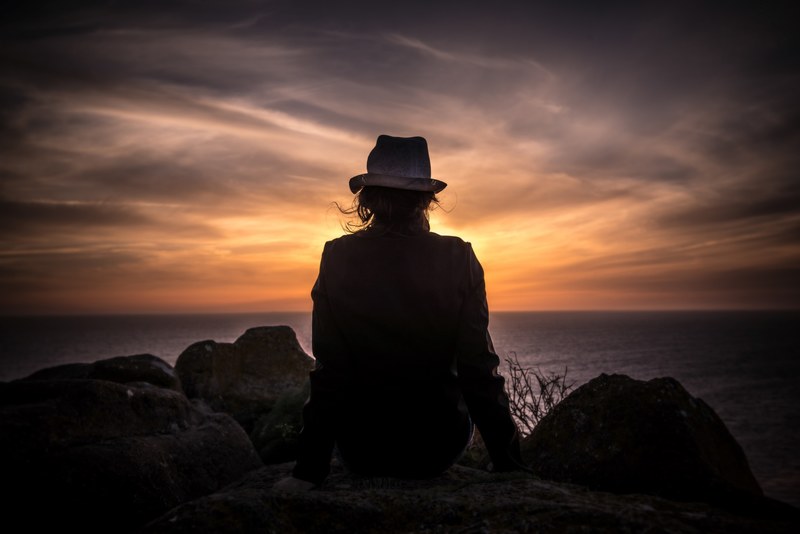 silhouette of a woman sitting on the edge of a cliff watching the sunset, _sunset silhouette 4k