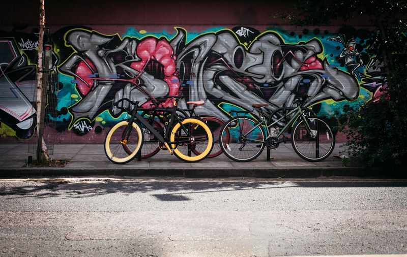 bikes parked on sidewalk in front of colorful graffiti mural on wall in shoreditch, bikes in front of graffiti wall 4k