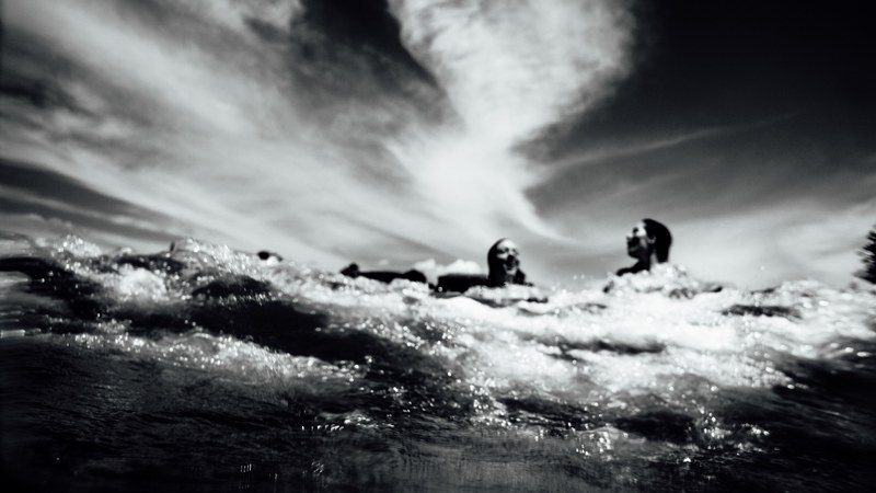 black and white shot of people having fun in water with clouds in sky mount maunganui, fun in water maunganui 4k