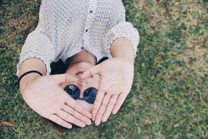 a woman laying on grass holds her hands up to make heart shape, hearts perspective 4k