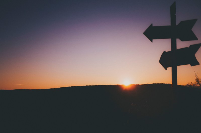 silhouette arrow signpost pointing to the left in cluj napoca as the sunrise or sunset illuminates the sky pale orange fading to blue, lost in the wilderness 4k