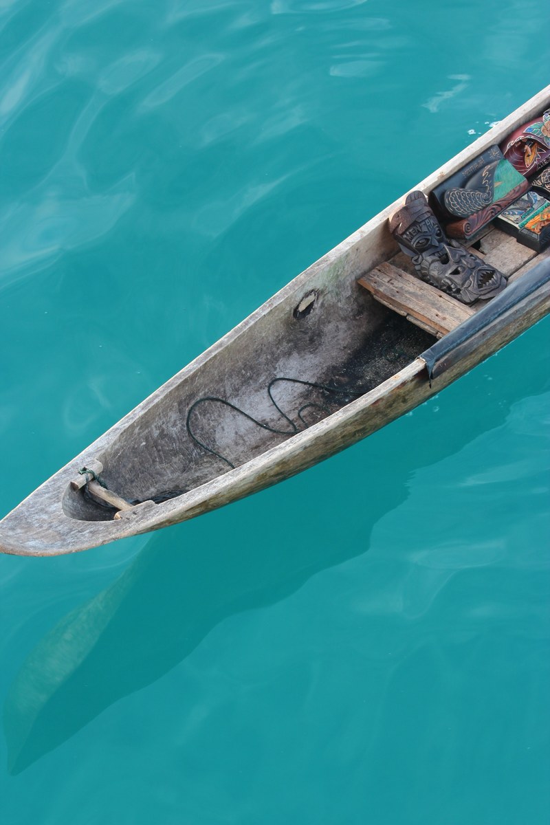 a wooden canoe with tribal masks inside on the azure surface of water, tribal canoe 4k