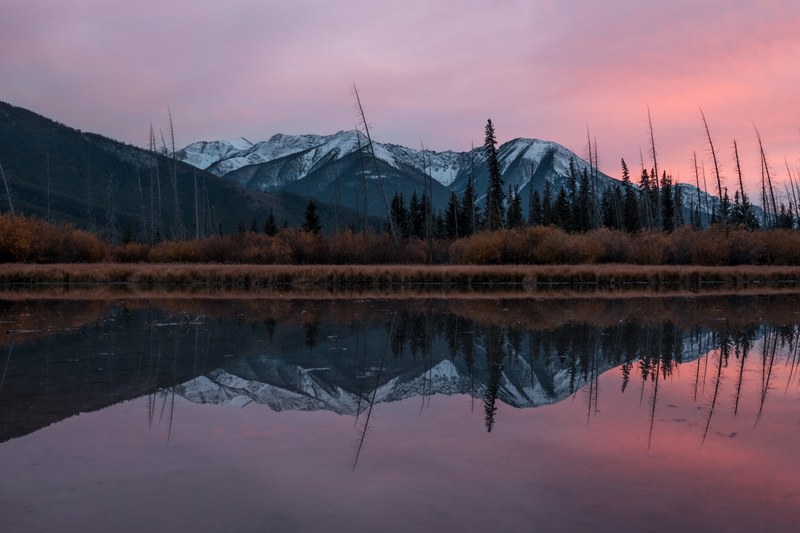 a snowcapped mountain range trees and cloudy skies are reflected in calm water as the sun sets, mountain tree sunset and sunrise 4k