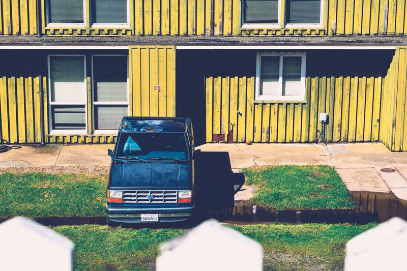 a blue truck with rust casts a shadow on the lawn of a yellow building, blue truck and yellow building 4k