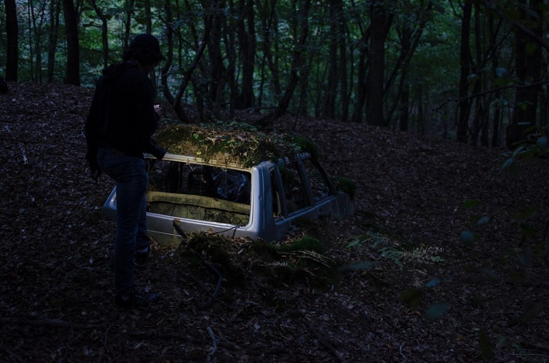 a person near an abandoned car half buried in dirt and leaves in a forest, man car moss leaves 4k