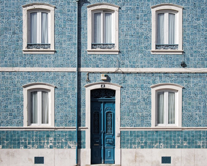 wall of a light blue house with three windows on the second level and two windows flanking a blue door, blue stone house with windows 4k
