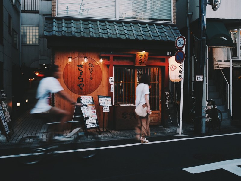 a woman walks past a small wooden shop as a cyclist speeds by, zen capital 4k