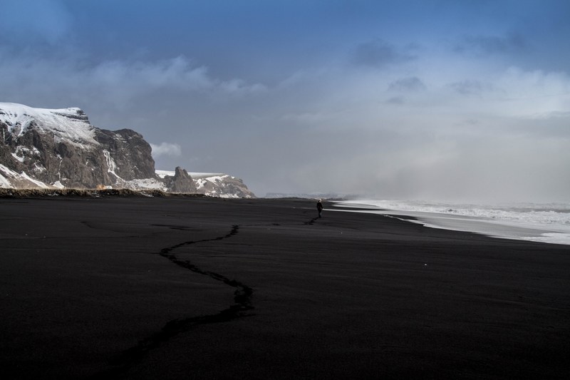 person walks alone on a volcanic beach in a mountain landscape, lonely beach walk 4k