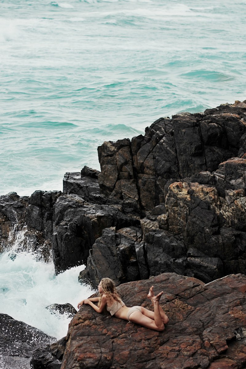 a woman lying on her stomach on the edge of a seaside cliff, _mermaid among the rocks 4k