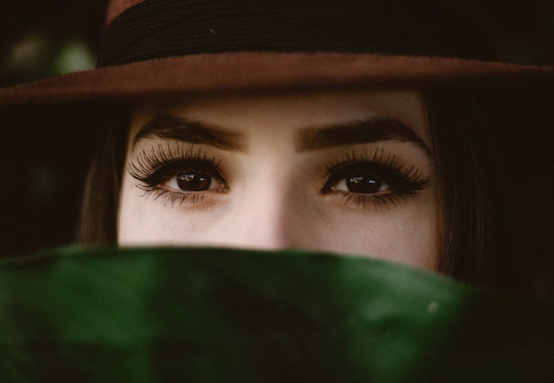 woman with bold eyebrows and dramatic lashes looking over a leaf, bold eye makeup 4k