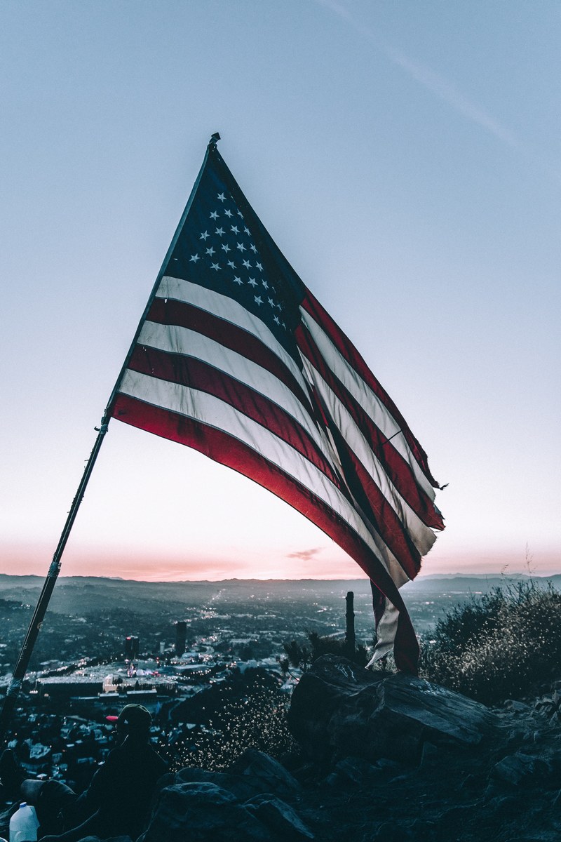 the american flag blowing in the wind off the side of a cliff in los angeles during sunset, make america american again 4k
