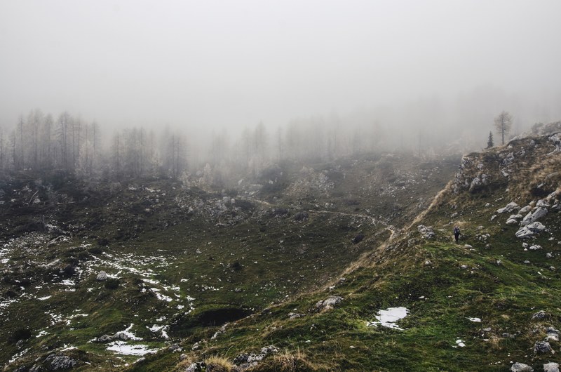 a lone hiker in a barren hilly landscape with snow covered trees on the horizon, exploring the desolate wilderness 4k