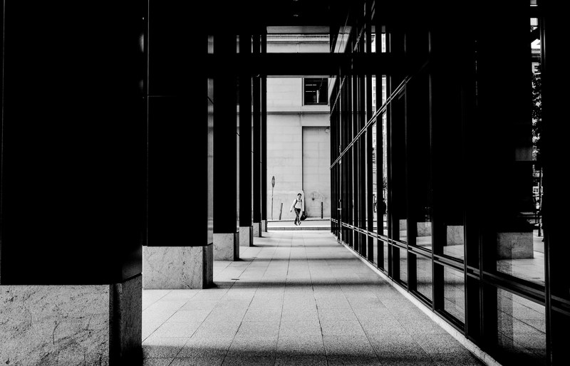 black and white long shot of man crossing road through outdoor corporate hallway in san francisco, monochrome corporate hall 4k