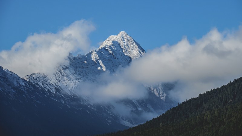 a snowy mountain peak rising up between thick clouds in leutasch, clouds and blue sky over a mountain 4k