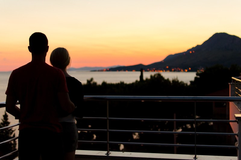 silhouetted lovers look out over the ocean from a landing in the hills above, from the hills to the sea 4k
