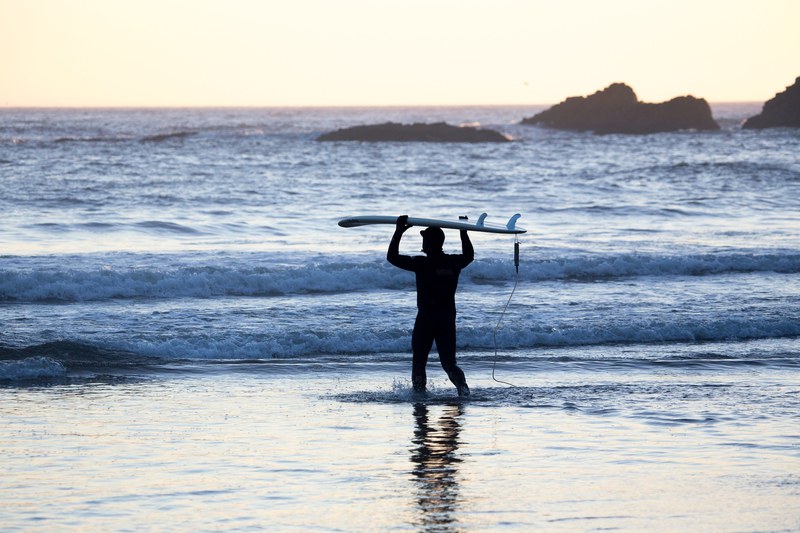 a silhouetted surfer carrying a board over his head walking towards the sea at sunrise or sunset, surfer entering the blue sea 4k