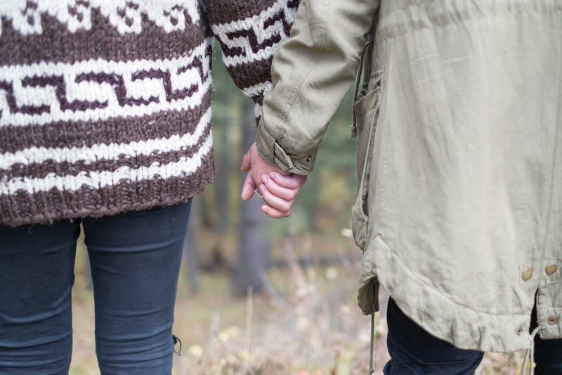 a couple wearing long sweaters with their backs to the camera holds hands against fuzzy background, holding hands in sweaters 4k