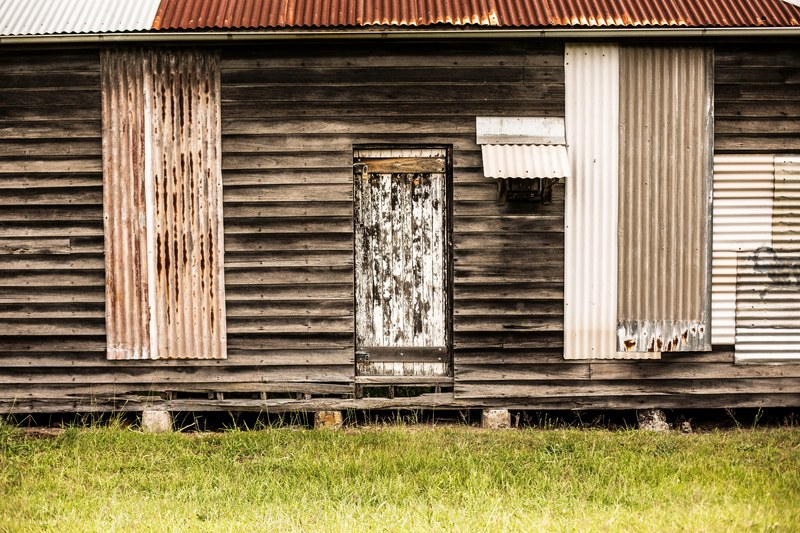 wooden cabin with tin sheet patches and a decaying door in a grassy lawn, old tin and wood cabin 4k